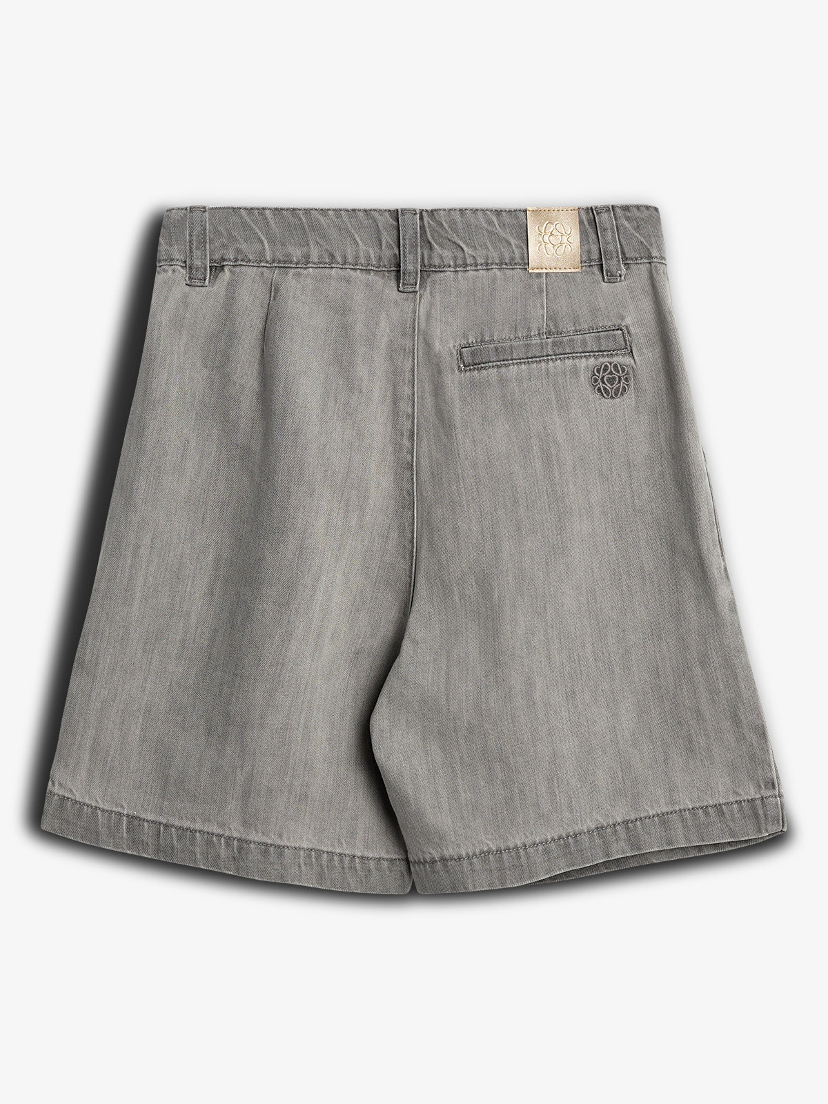 Kurze graue Shorts liegen flach, zeigen Gesäßtasche mit Sticklogo. Ein kleines Etikett mit stilisiertem Logo ist sichtbar. Der Hintergrund ist einfarbig grau.