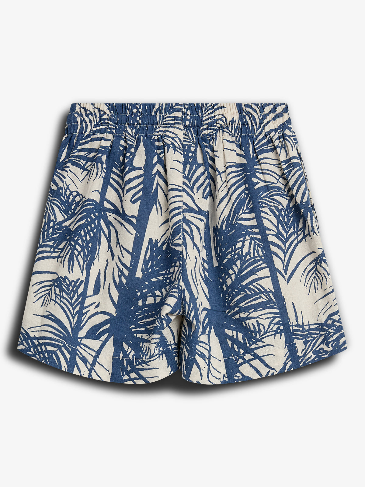 Kurze Hose mit Palmenmuster, in Blau und Weiß gestaltet. Sie hängt locker und hat einen elastischen Bund. Der Hintergrund ist ein einfarbiger, heller Raum.