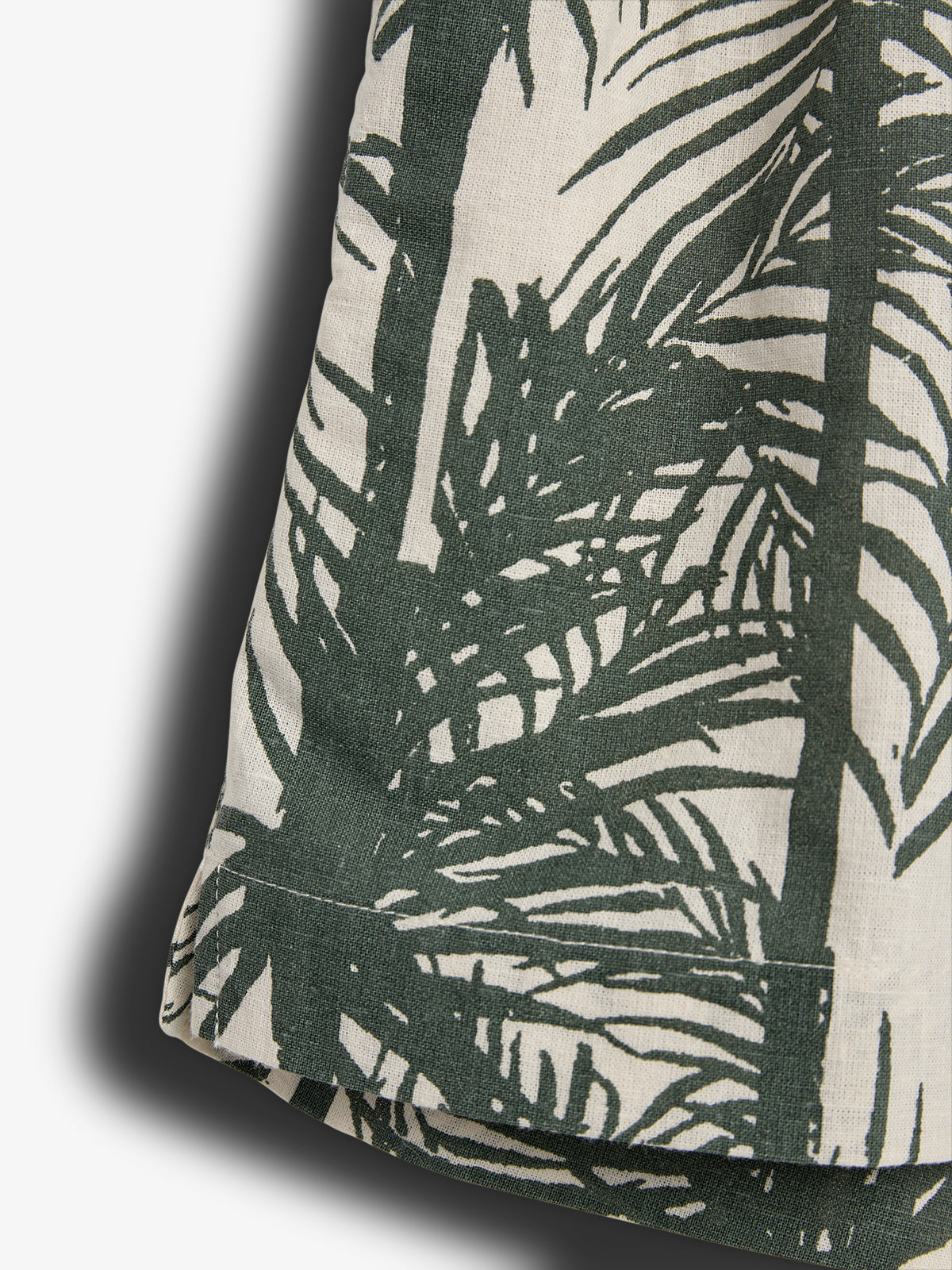 Fabric featuring dark green tropical palm leaf prints on a beige background, draped and casting a shadow, suggesting a stylish, natural-themed textile design.
