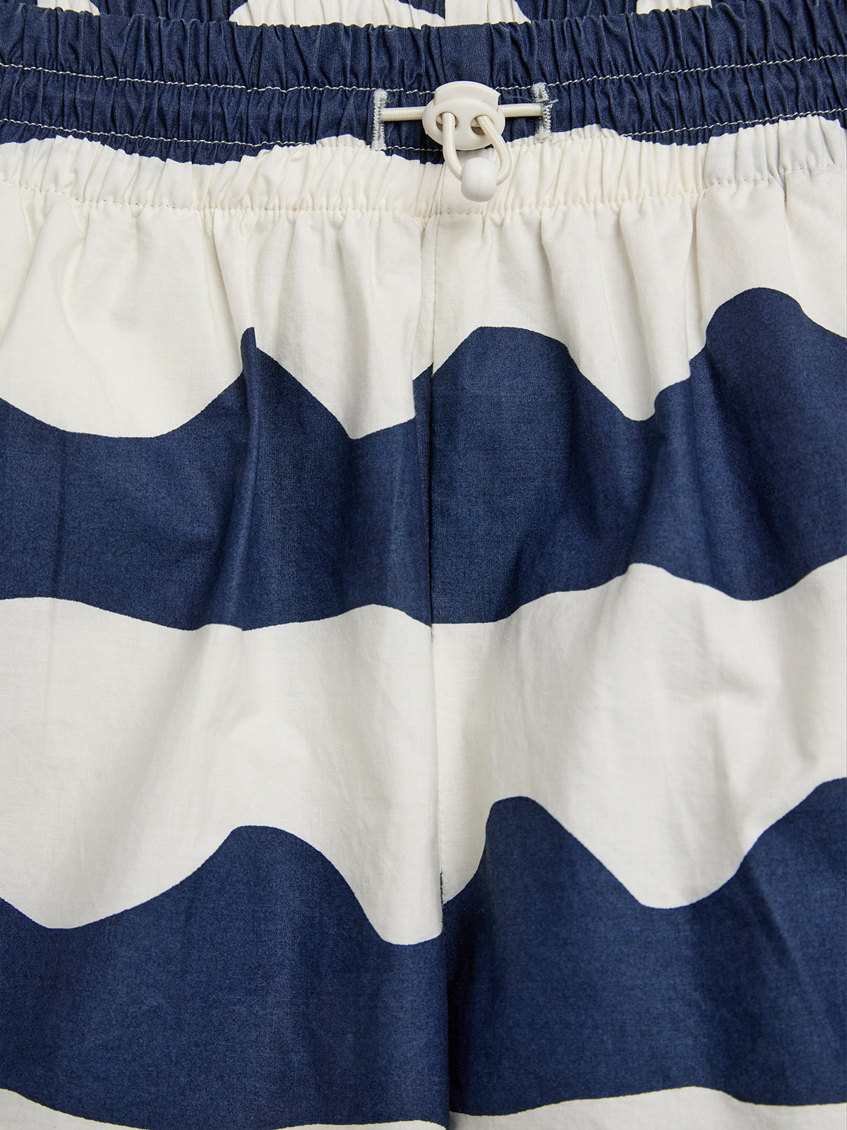 Kurze Hose mit blau-weißem Zickzackmuster. Ein weißer Kordelzug zur Anpassung. Hintergrund aus demselben Stoff, ohne zusätzlichen Kontext oder Text.