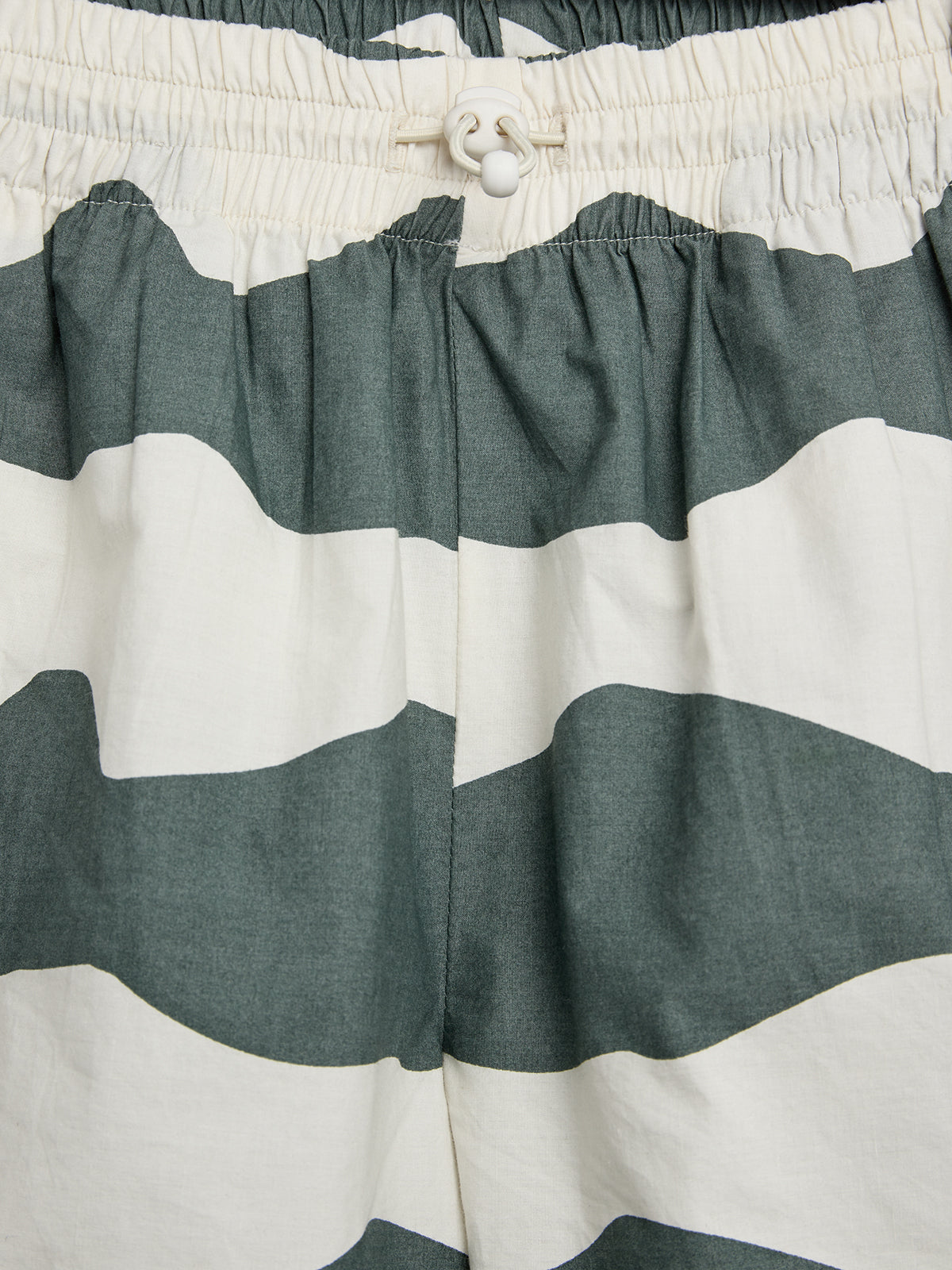 Kurze Hose mit grau-weißen Streifen, elastischem Bund und Kordelzug, vor einem neutralen Hintergrund dargestellt.