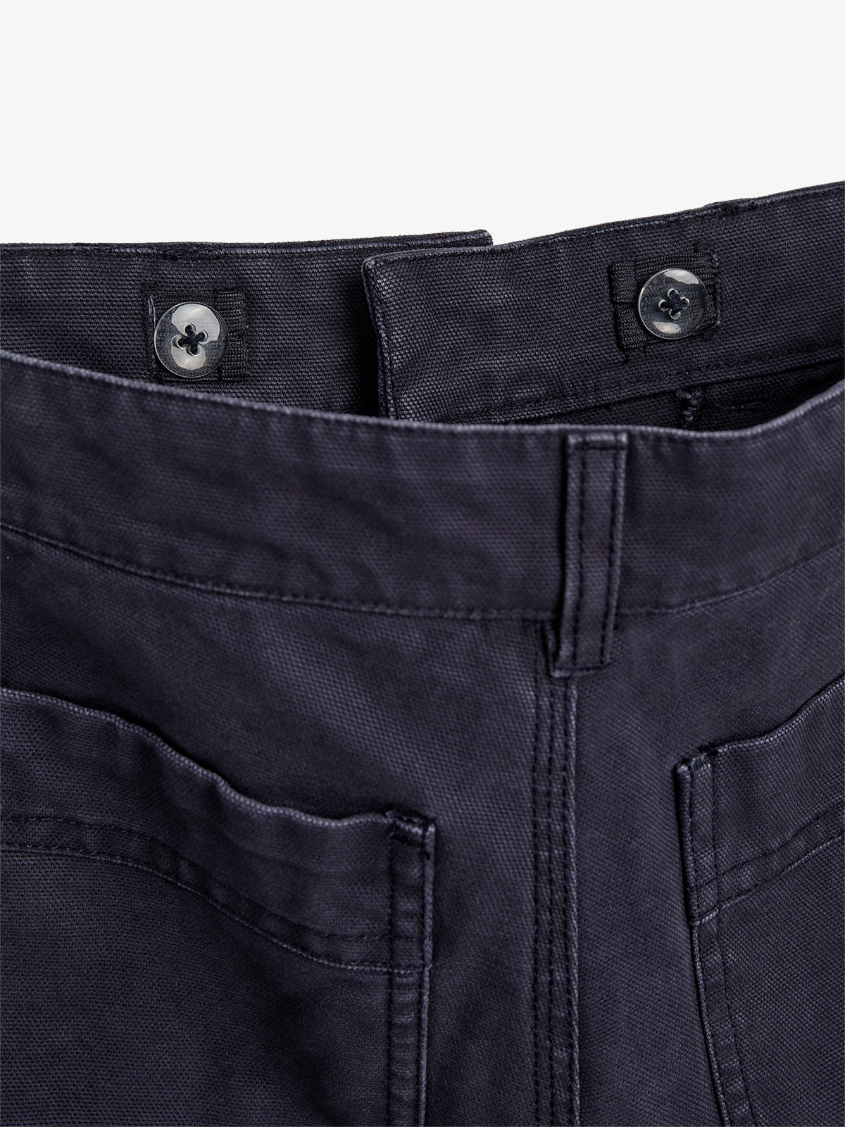 Dunkelblaue Hose, geschlossen mit zwei dunkelgrauen Knöpfen, liegt flach. Der Fokus liegt auf dem oberen Teil mit Gürtelschlaufen, vor weißem Hintergrund.