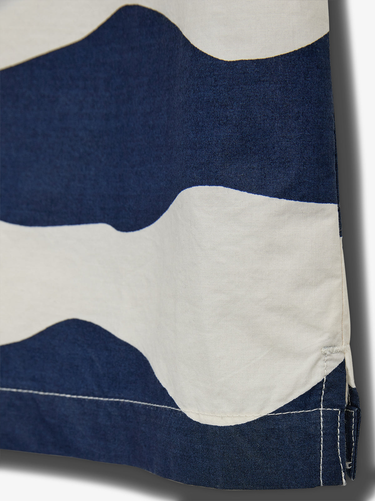Ein wellenförmiger Stoff in Blau und Weiß hängt glatt, mit sauber genähten Kanten im Fokus. Hintergrund ist neutral, hebt das Muster hervor.