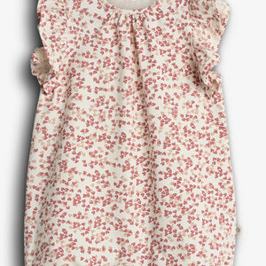 Ein Babystrampler mit rot-weißen Blümchenmuster, verziert mit Rüschen an Schultern und Ärmeln, auf weißem Hintergrund. Text auf dem Etikett: „Pehr LULI ORGANIC COTTON“.