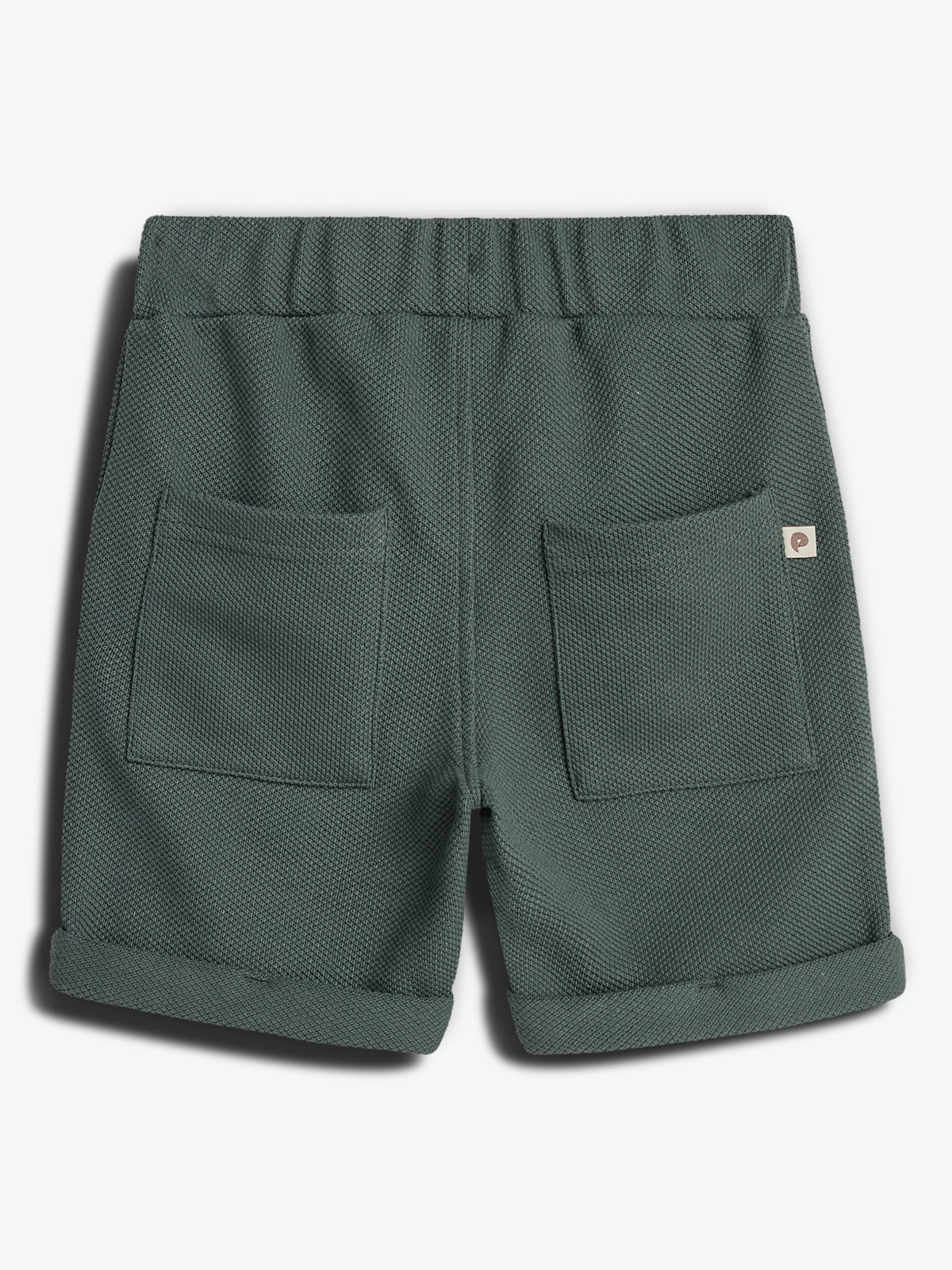 Kurze Hose mit elastischem Bund und zwei großen aufgesetzten Taschen. Der Stoff hat eine Textur und ist dunkelgrün. Die Hose liegt auf einer weißen Oberfläche.