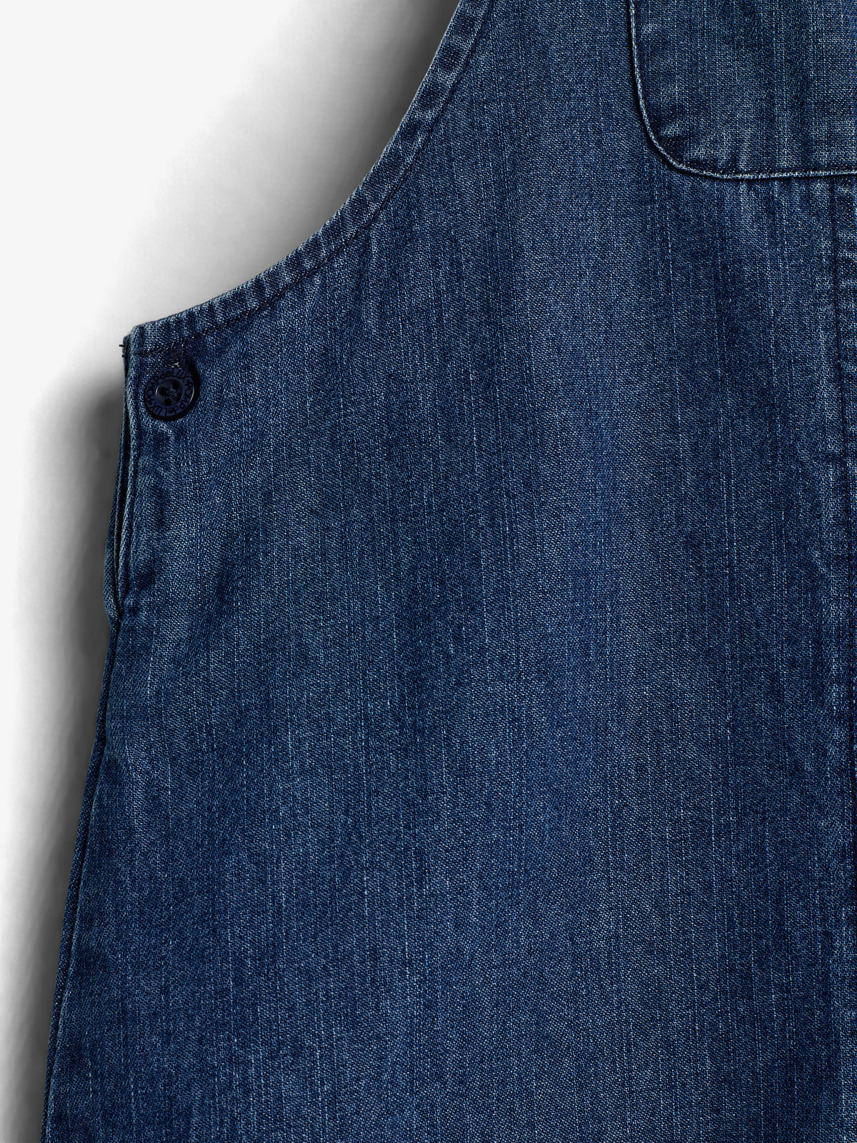 Blauer Denim-Stoff, ruhig an einer Wand hängend, mit einem Knopf sichtbar in der oberen Ecke und gezielten Nähten, die Struktur und Design im Gewebe betonen.