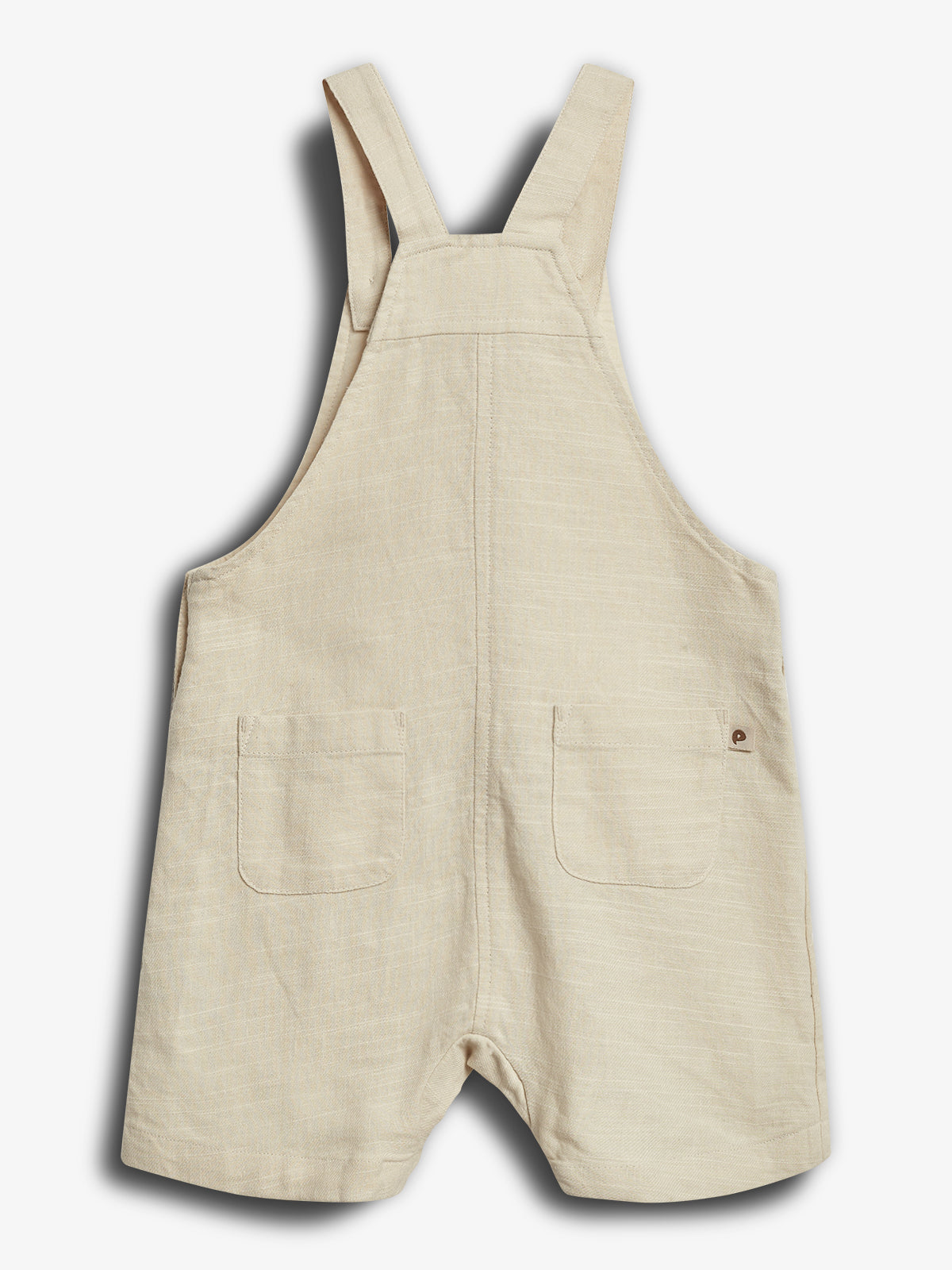 Beige-Overall aus Leinen mit zwei aufgesetzten Taschen, die auf einer flachen Fläche liegen. Die Träger sind gerade und breit, geeignet für Kleinkinder.