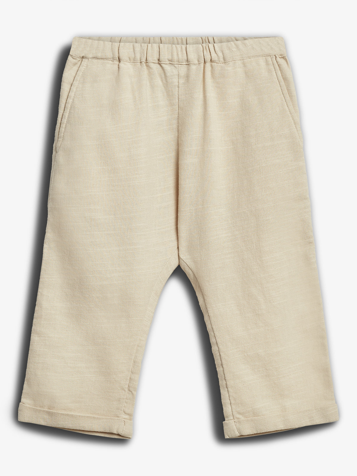 Eine beige Kinderhose liegt flach ausgebreitet, mit elastischem Bund und zwei Seitentaschen. Die Hosenbeine sind gerade geschnitten. Hintergrund ist eine neutrale, weiße Fläche.