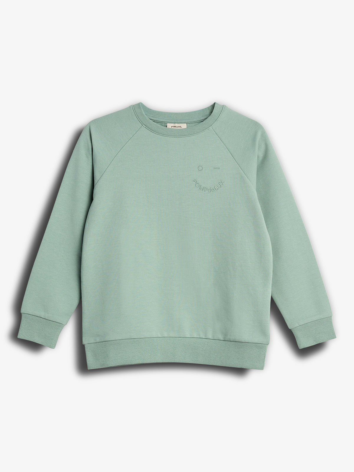 Ein hellgrüner Pullover liegt flach vor einem weißen Hintergrund. Oben rechts ist ein dezentes Gesichtsmotiv mit dem Text "Bonjour." sichtbar.
