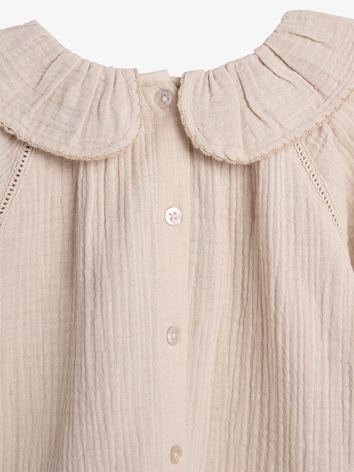 Beige, textured blouse with a round collar and vertical buttons, displayed flat with intricate stitching details, set against a plain white background.