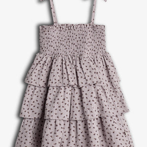 A sleeveless, tiered dress with spaghetti straps and bow detailing. It features a smocked bodice and a floral pattern on a light fabric, set against a plain background.