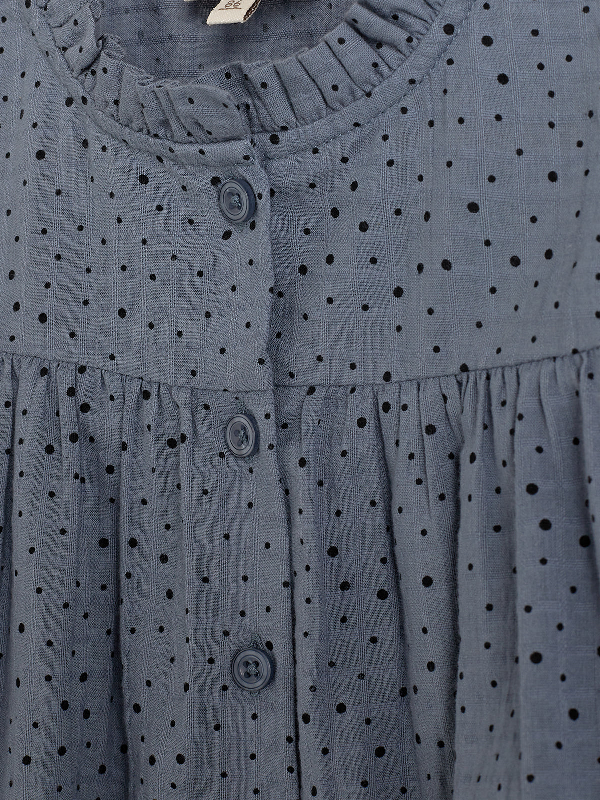 Graues Kleid mit schwarzen Punkten und Knopfleiste. Der Stoff hat ein geräumiges Faltenmuster, das der Kleidung eine luftige Struktur verleiht. Der Hintergrund ist neutral und unsichtbar.