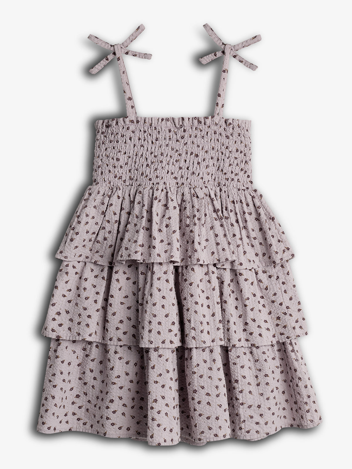 Ein ärmelloses, geblümtes Kleid mit gerafftem Oberteil und volantartigem Rock hängt vor einem weißen Hintergrund. Die Träger sind mit Schleifen gestaltet, was dem Kleid einen verspielten Look verleiht.