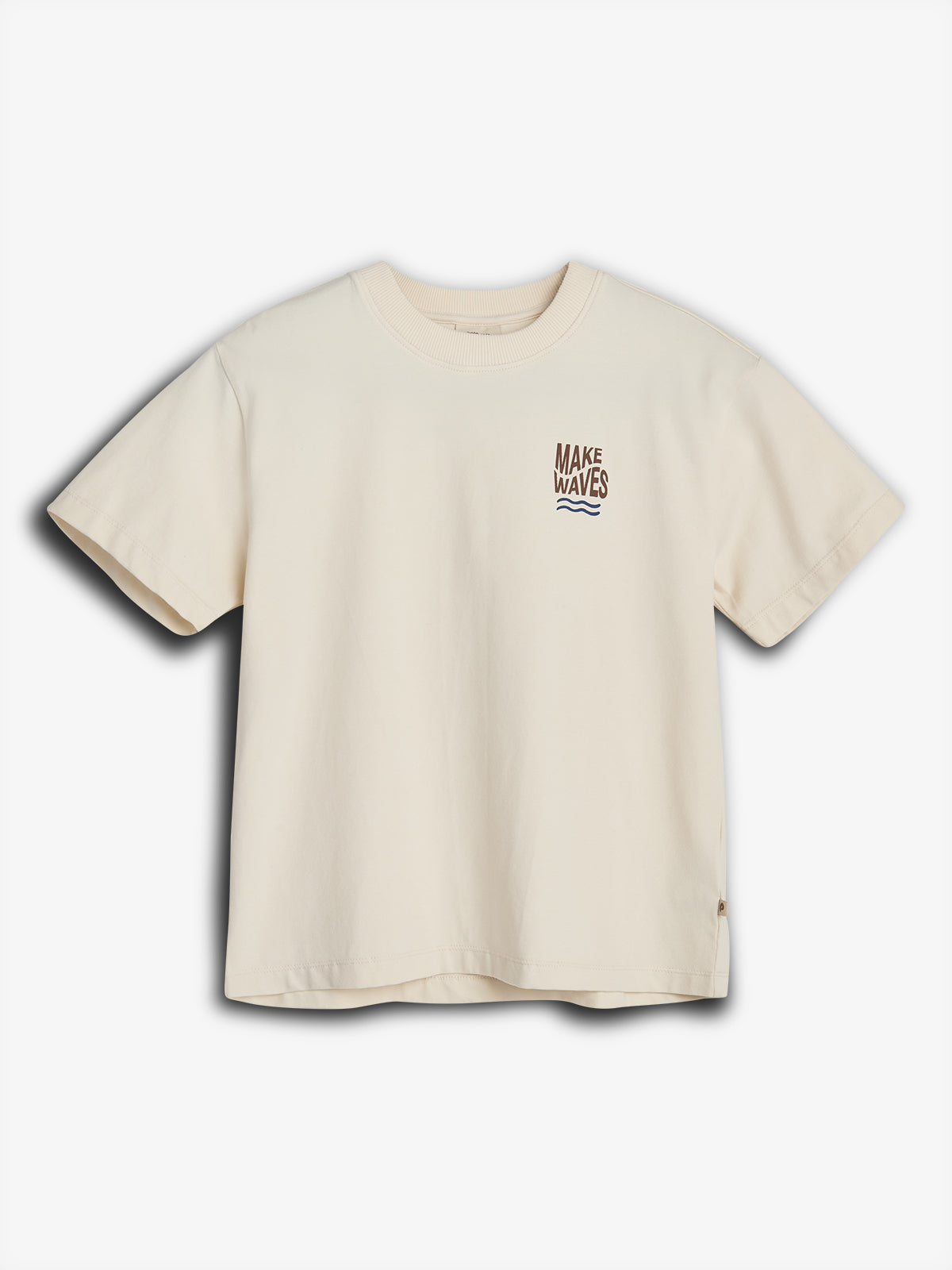 Ein cremefarbenes T-Shirt zeigt den Text "MAKE WAVES" über einer kleinen Wellengrafik. Das T-Shirt liegt flach auf einer weißen Oberfläche ohne weitere Objekte im Hintergrund.
