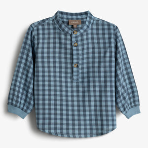 Ein kariertes Hemd mit langen Ärmeln, Hemdkragen und drei Knöpfen vorne; im Hintergrund eine weiße Fläche. Auf dem Etikett steht: "POMP DE LUX. 86".