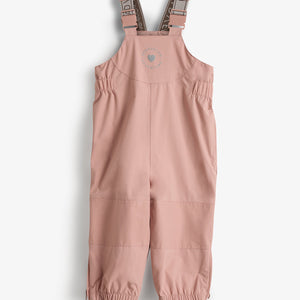 Eine rosa Kinder-Regenhose mit verstellbaren Trägern hängt vor weißem Hintergrund. Sie hat elastische Beinabschlüsse und runde Markierung auf der Brust mit dem Text: "EXPLORER ADVENTURE".