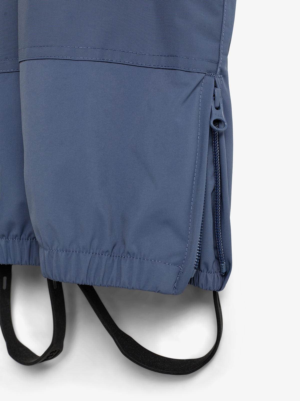 Eine blau-graue Hose mit einem Reißverschluss an der Seite und elastischen Bündchen. Unten sind schwarze, elastische Gummiriemen angebracht. Der Hintergrund ist neutral weiß.