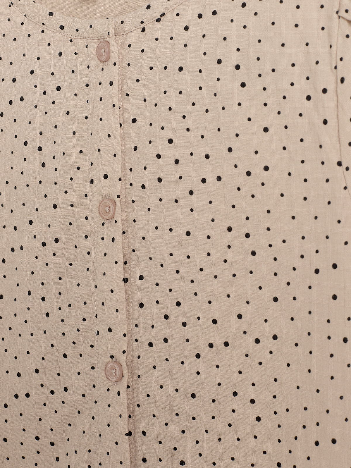 Beigefarbene Bluse mit schwarzen Punkten und Knopfleiste vorne. Die Knöpfe verlaufen senkrecht die Mitte hinunter. Der Stoff hat eine leichte Textur, die Punkte sind gleichmäßig verteilt.