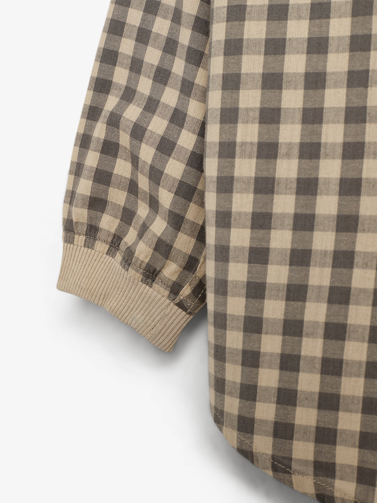 Ein Hemdärmel mit kariertem Muster bewegt sich leicht nach unten. Der Stoff besteht aus beigen und braunen Quadraten, während das Bündchen aus einem elastischen Strickmaterial besteht.