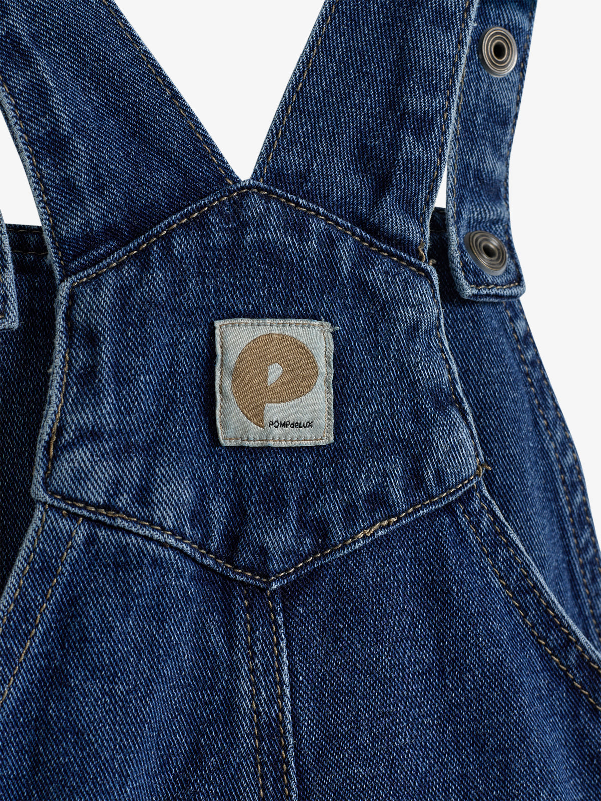 Ein Jeanslatz zeigt Nähte und Ösen, aufgenähtes Etikett mit Logo "POMPdeLUX" in hellem Quadrat, in Nahaufnahme ohne sichtbare Umgebung.
