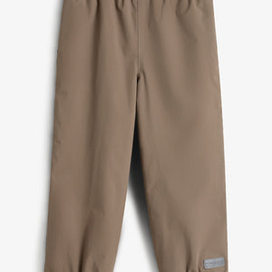 Eine braune, knöchellange Hose mit elastischem Bund und Beinabschlüssen liegt flach ausgebreitet auf einem weißen Hintergrund. Ein graues Etikett mit der Aufschrift "POM POMPS" befindet sich am unteren Rand.