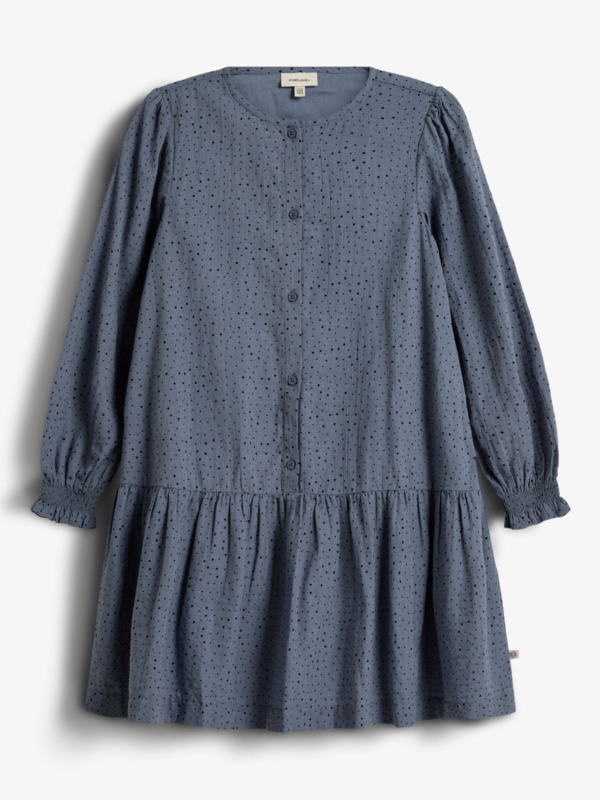 Ein langärmliges, blaues Kleid mit Knopfleiste und Rüschen am Saum hängt vor einem weißen Hintergrund. Das Kleid hat ein Lochmuster. Text: "PINAR AKS" und "110".