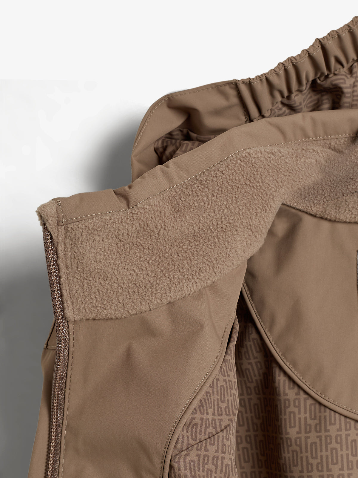 Braune Jacke mit weichem Futter. Sie hängt offen, wodurch das gemusterte Innenfutter sichtbar wird. Die äußere Oberfläche ist glatt, der Reißverschluss an der linken Seite.