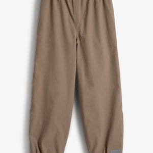 Eine braune Regenhose mit elastischem Bund und Beinabschlüssen liegt auf weißem Hintergrund. Unten rechts ist ein graues Etikett mit der Aufschrift „Polarn O. Pyret“ zu sehen.