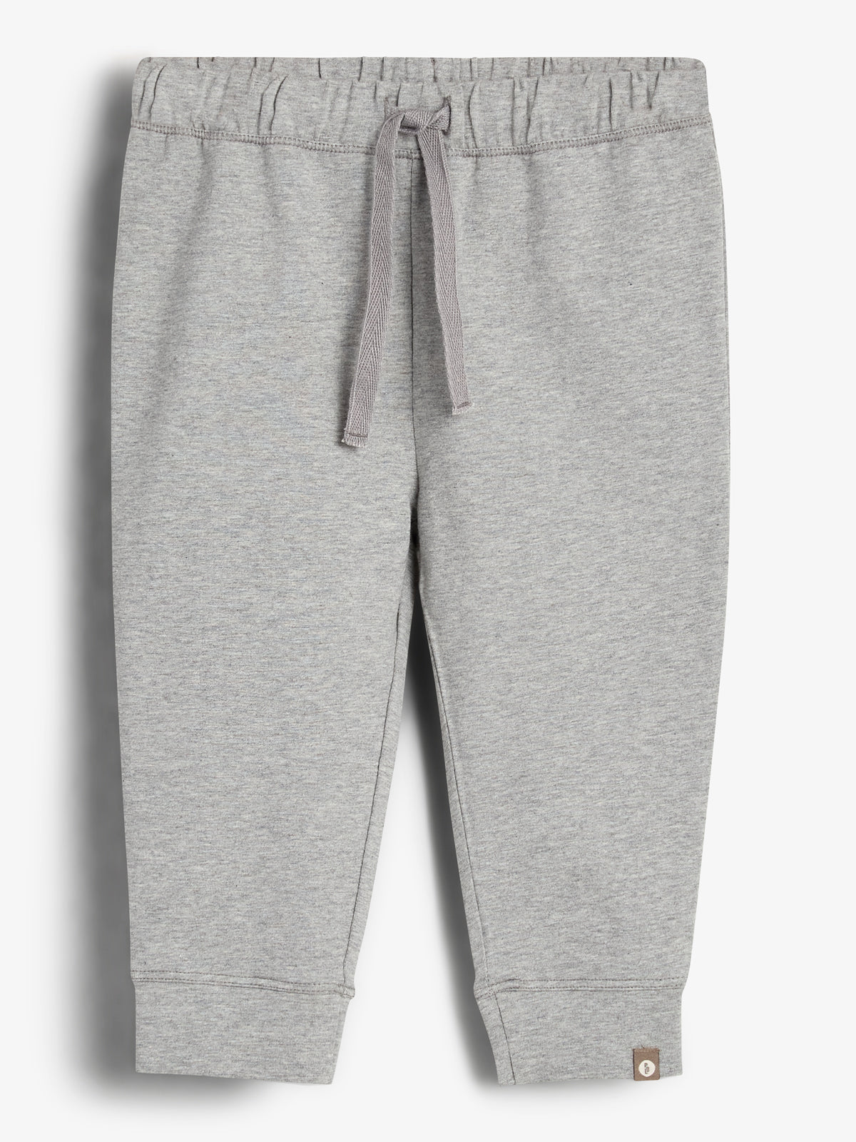 Graue Jogginghose mit Kordelzug in der Taille, liegend auf weißem Hintergrund. Die Hose hat elastische Bündchen und ein kleines Etikett am unteren Rand des linken Beins.