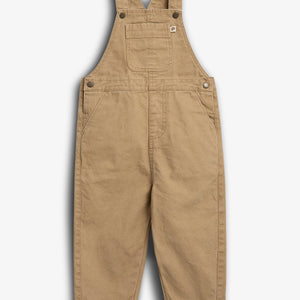 Latzhose aus braunem Stoff hängt gerade, mit Hosenträgern und Bauchtasche. Der helle Hintergrund lässt die Nähte und Knöpfe deutlich hervortreten. Ein kleines Etikett ist sichtbar.