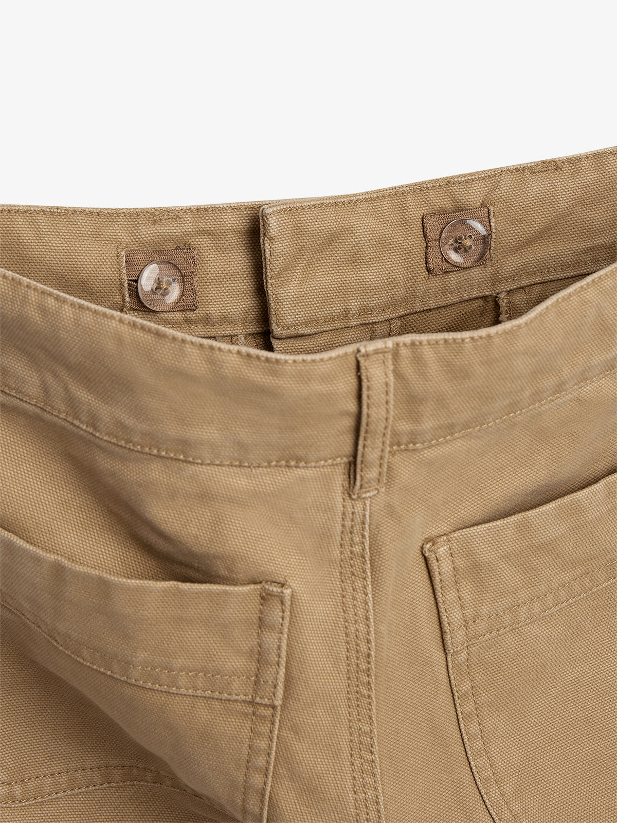 Beigefarbene Hose, geknöpft an der oberen Naht, zeigt Detail der Taschen und Nähte. Die Hose liegt flach in einem neutralen Raum.