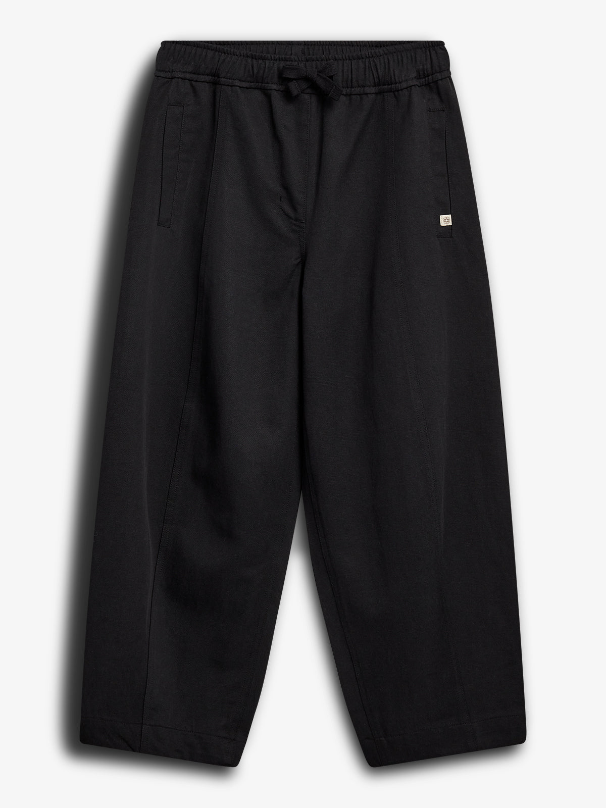 Schwarze Hose mit elastischem Bund und Kordelzug, stilvoll und minimalistisch, vor einem einfachen weißen Hintergrund präsentiert. Zwei seitliche Taschen und ein kleines Logo-Label sind sichtbar.