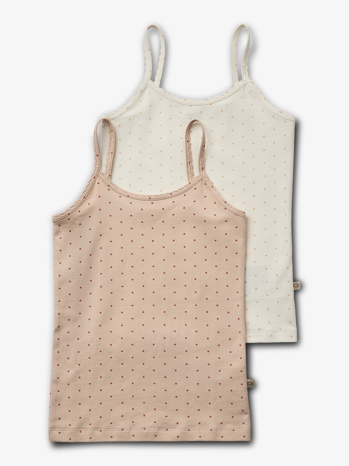 Zwei Trägertops liegen übereinander; das vordere ist beige, das hintere weiß, beide mit kleinen Punkten verziert. Der Hintergrund ist neutral gehalten, ohne zusätzliche Details.