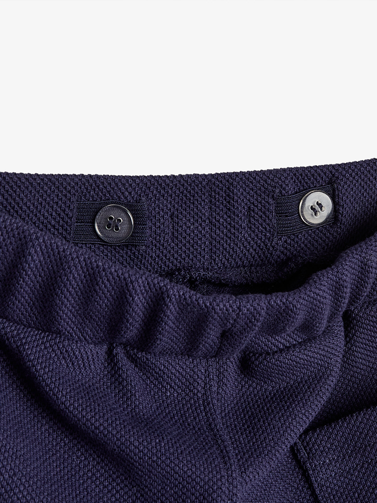 Dunkelblauer, gerippter Stretchbund mit zwei Knöpfen sitzt auf einer Hose; der Detailausschnitt zeigt Textur und Nähte in Nahaufnahme vor einem weißen Hintergrund.