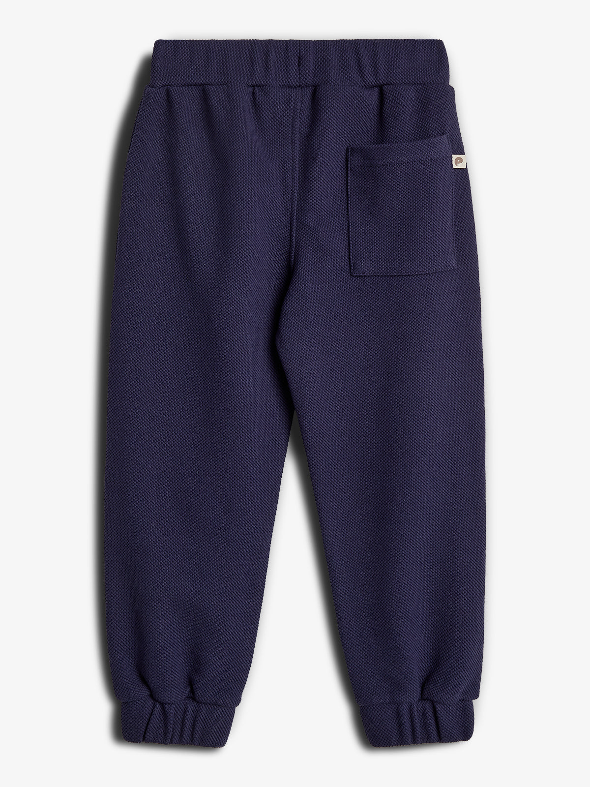 Eine dunkelblaue Kinderhose liegt flach auf einem hellen Hintergrund. Sie hat eine elastische Taille, Bündchen am Saum und eine aufgesetzte Tasche auf der rechten Seite.