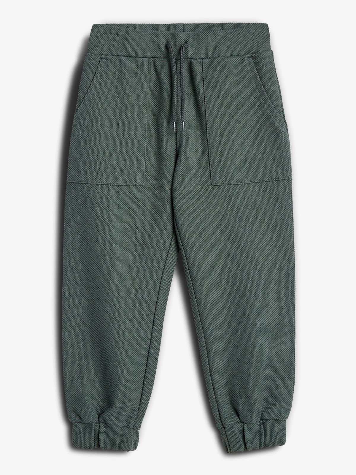 Eine grüne Jogginghose liegt flach auf weißem Hintergrund. Sie hat einen elastischen Bund mit Kordelzug, zwei aufgesetzte Taschen und gerippte Bündchen an den Beinabschlüssen.