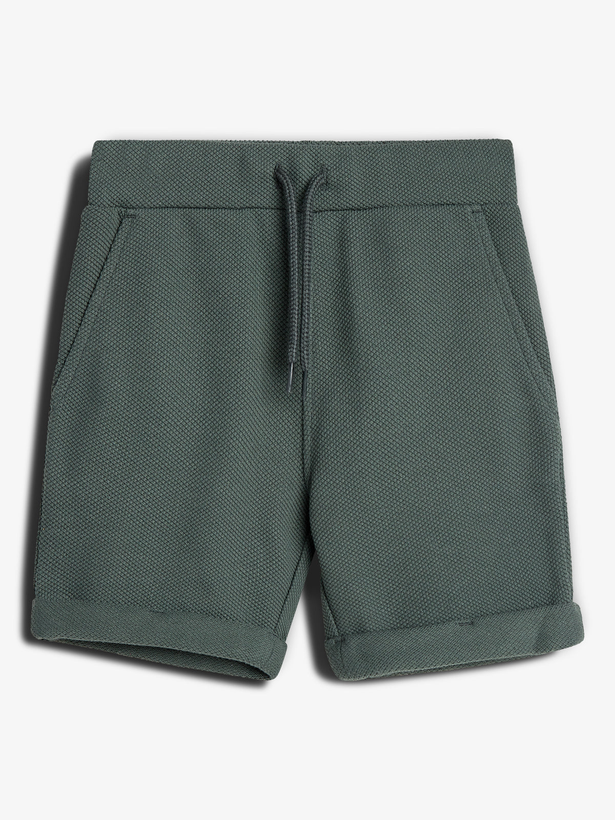 Eine grüne, kurze Hose mit Kordelzug liegt flach auf einem weißen Hintergrund. Sie hat aufgesetzte Taschen und umgeschlagene Beinenden, aus strukturiertem Stoff.