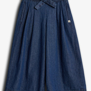 Ein blauer Jeansrock mit weitem Schnitt, elastischem Bund und Bindegürtel liegt flach. Er hat zwei Seitentaschen und ein kleines, quadratisches Etikett auf der linken Seite.