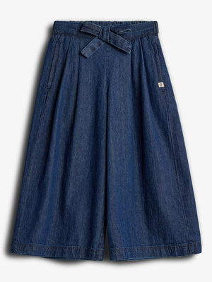 Ein blauer Jeansrock mit weitem Schnitt, elastischem Bund und Bindegürtel liegt flach. Er hat zwei Seitentaschen und ein kleines, quadratisches Etikett auf der linken Seite.