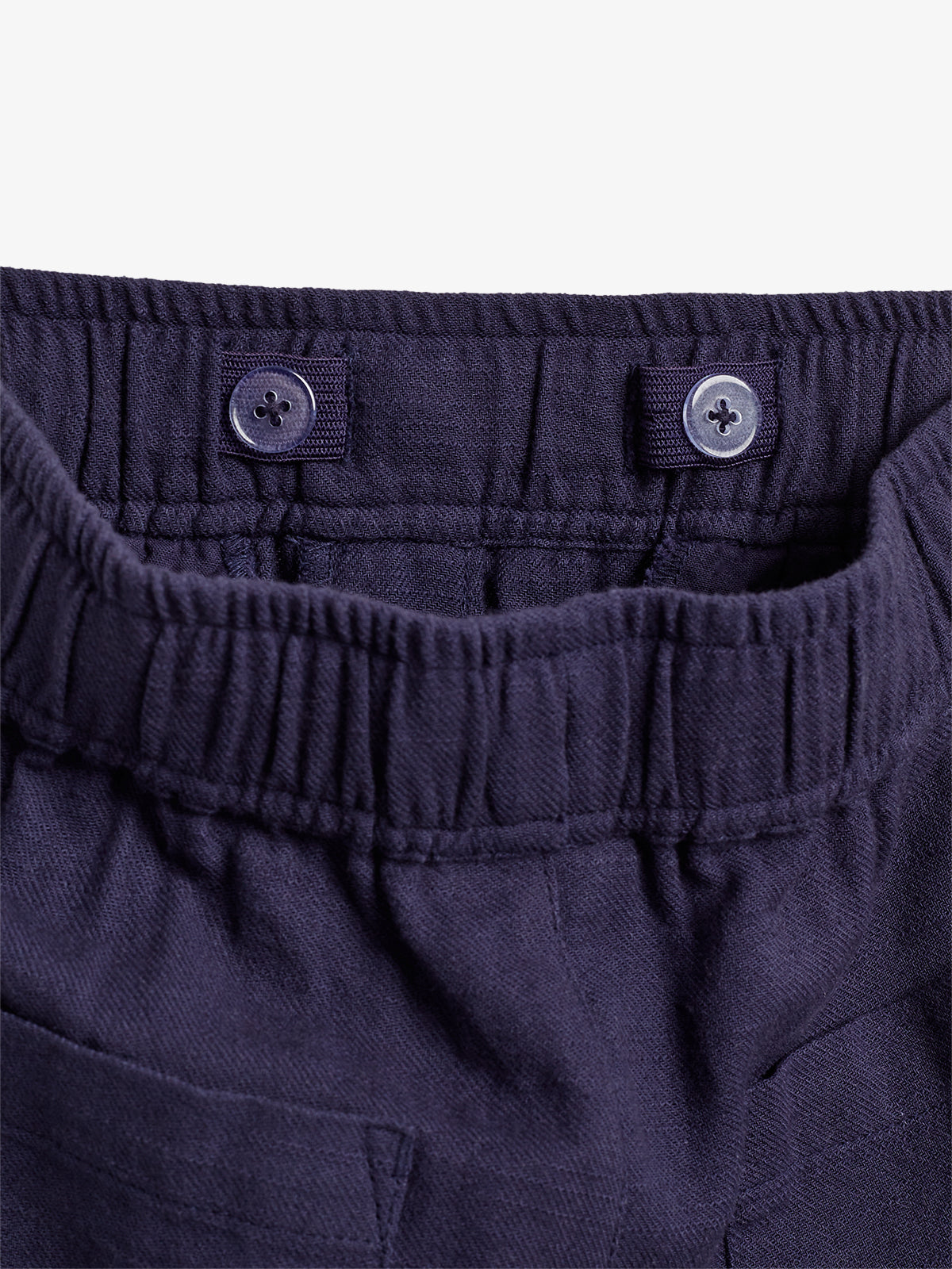 Dunkelblaue Hose mit elastischem Bund und zwei kleinen Knöpfen zur Anpassung. Im Vordergrund ist die obere Partie der Hose zu sehen, umgeben von einem hellen Hintergrund.
