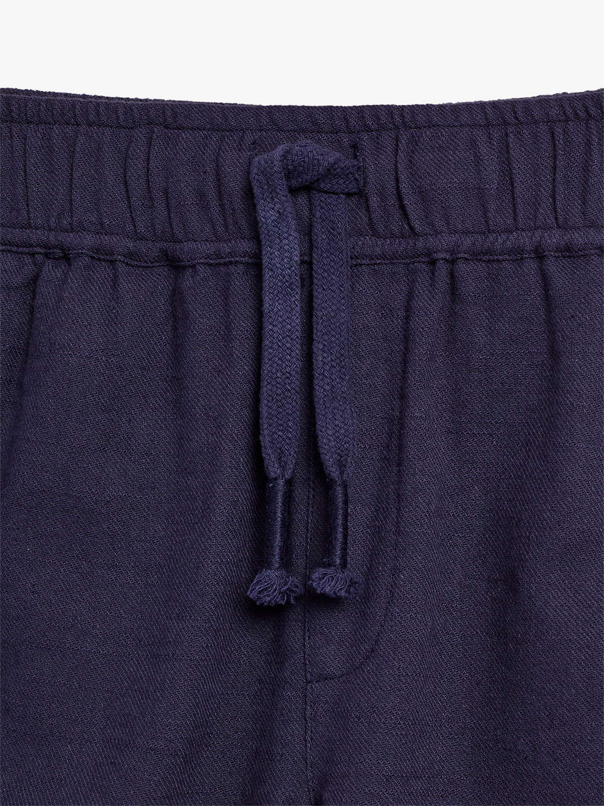 Dunkelblaue Hose mit Kordelzug an der Taille, locker zusammengebunden; der Stoff hat eine strukturierte Textur. Der Fokus liegt auf dem oberen Teil der Hose vor einem weißen Hintergrund.