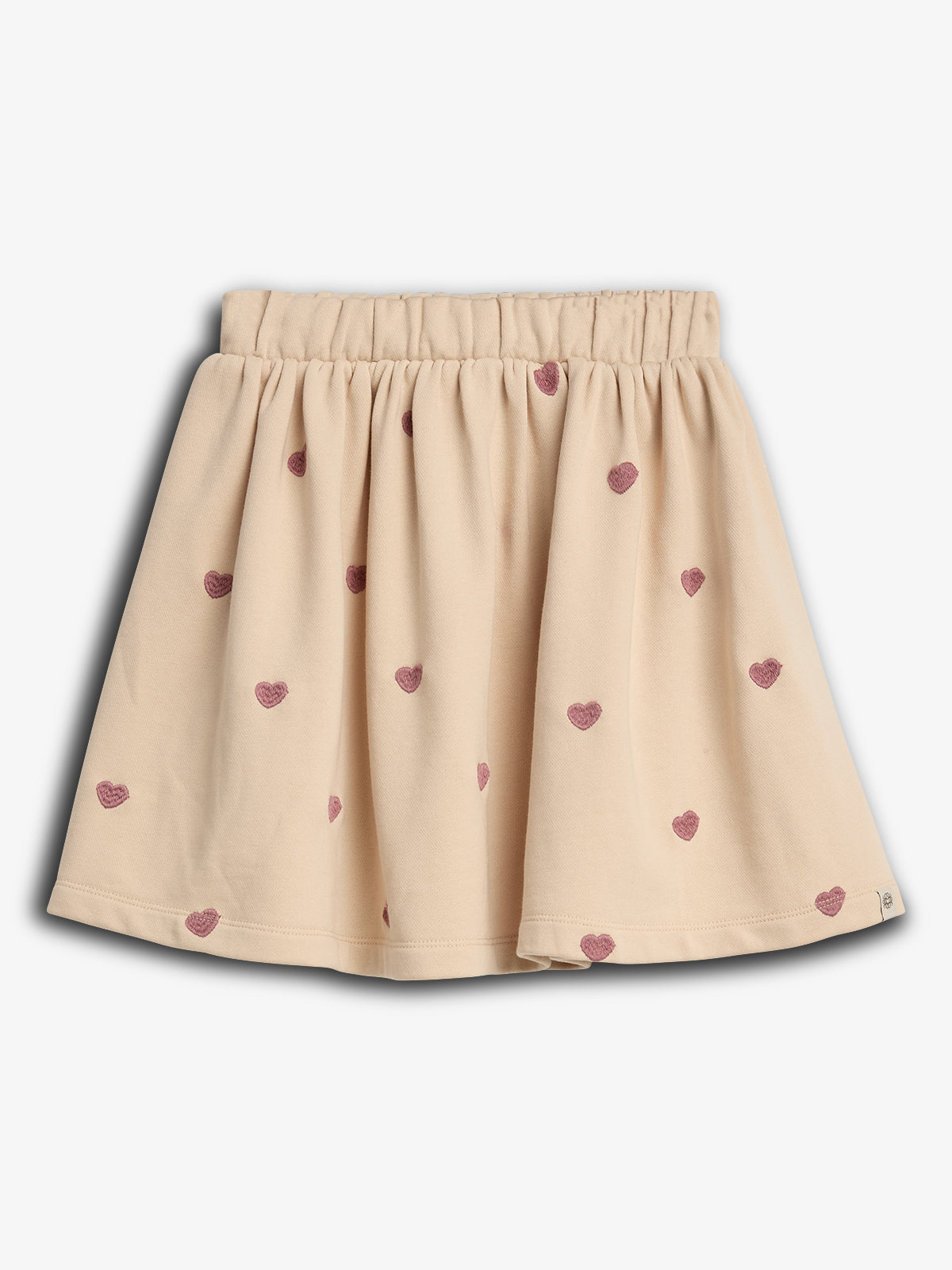 Ein beiger Kinderrock mit rosa Herzmustern verteilt. Der Rock hat einen elastischen Bund und fällt locker. Der Hintergrund ist neutral ohne weitere Dekoration.
