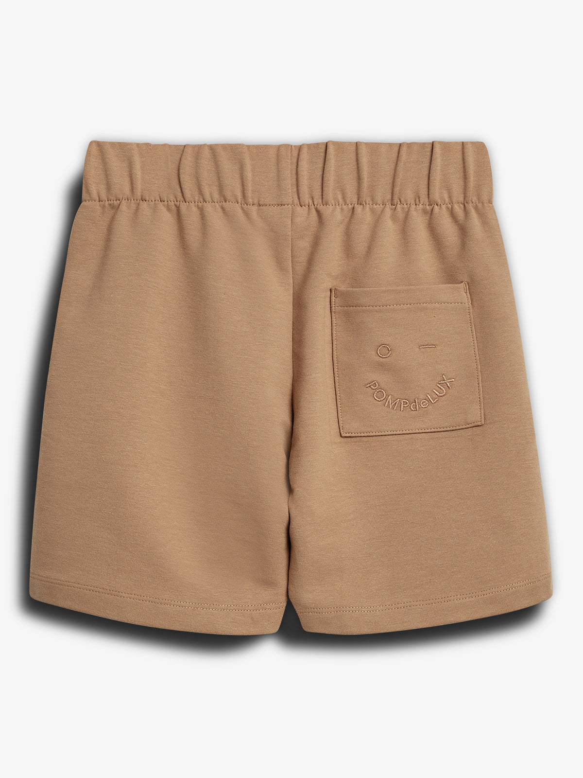 Beige Shorts mit elastischem Bund, einer aufgesetzten Tasche auf der Rückseite. Text auf der Tasche: "POMPdeLUX". Im Hintergrund ist ein neutraler, weißer Raum.