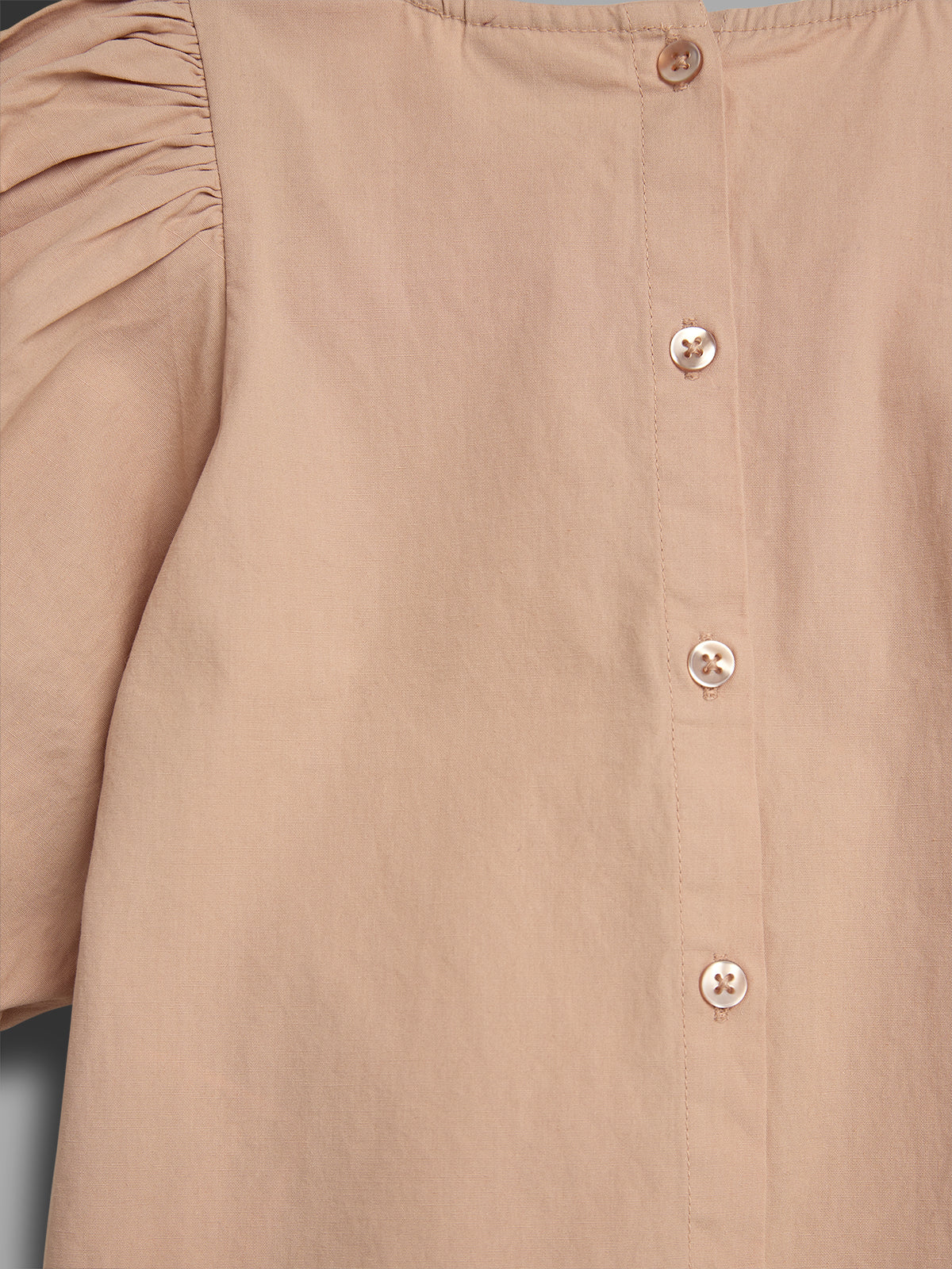 A beige shirt with puffed sleeves and five buttons vertically aligned along the back. The surrounding background is neutral and plain.