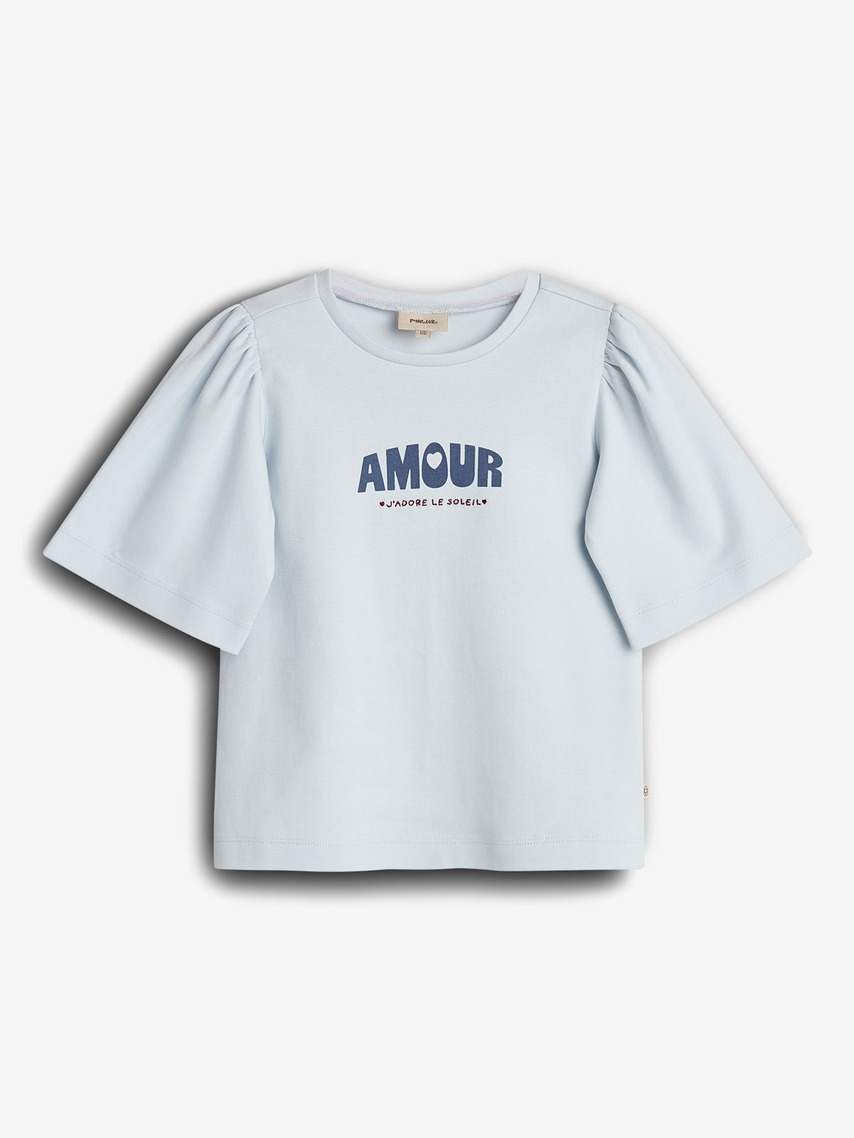 Ein hellblaues T-Shirt mit puffigen Ärmeln zeigt den Aufdruck "AMOUR J'ADORE LE SOLEIL" in blauer Schrift. Es liegt auf einem weißen Hintergrund.