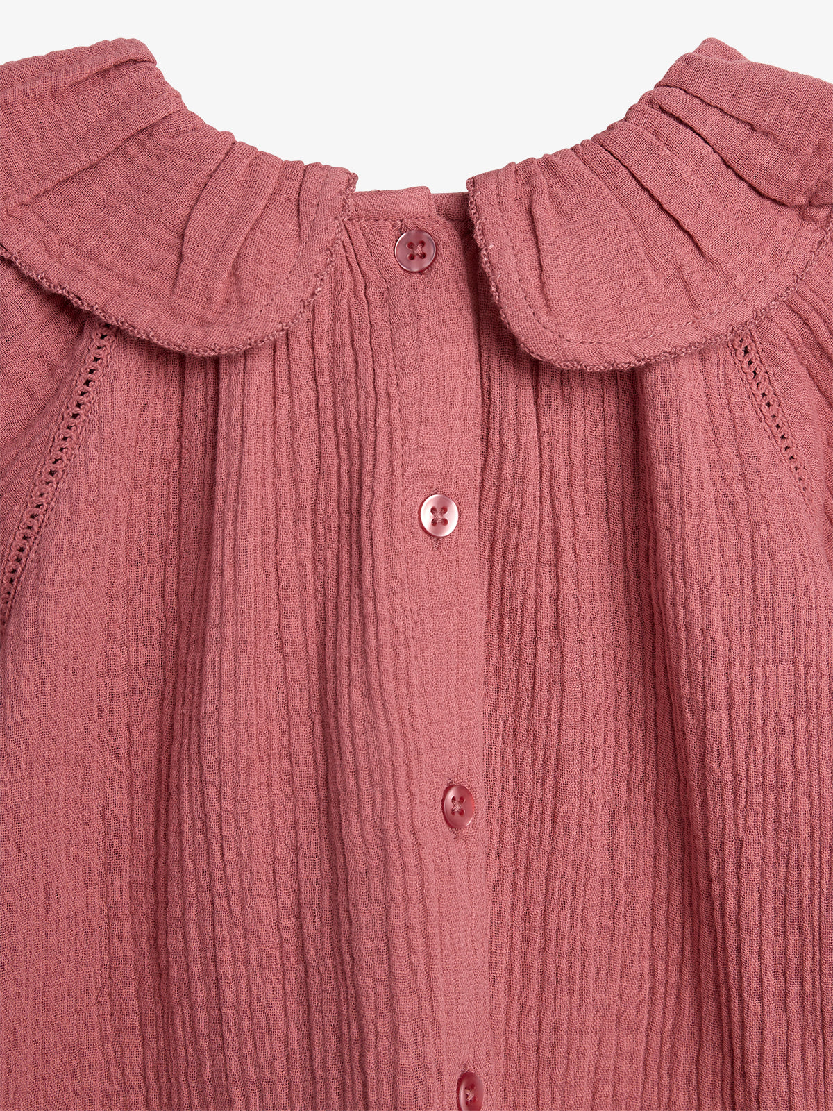A textured, pink fabric blouse features a rounded collar and vertical button fastenings down the front, set against a plain background.