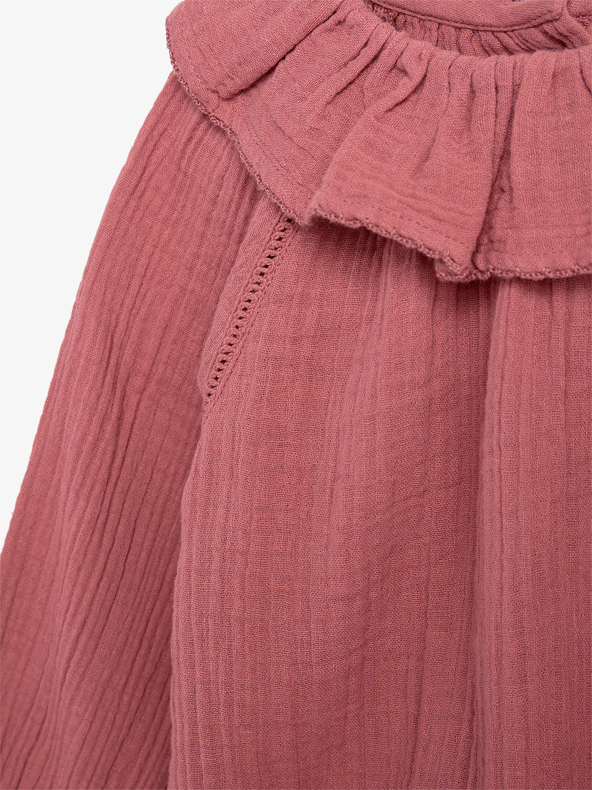 A close-up of a pink, crinkled fabric blouse featuring a ruffled collar, highlighting texture and detail without visible background context.