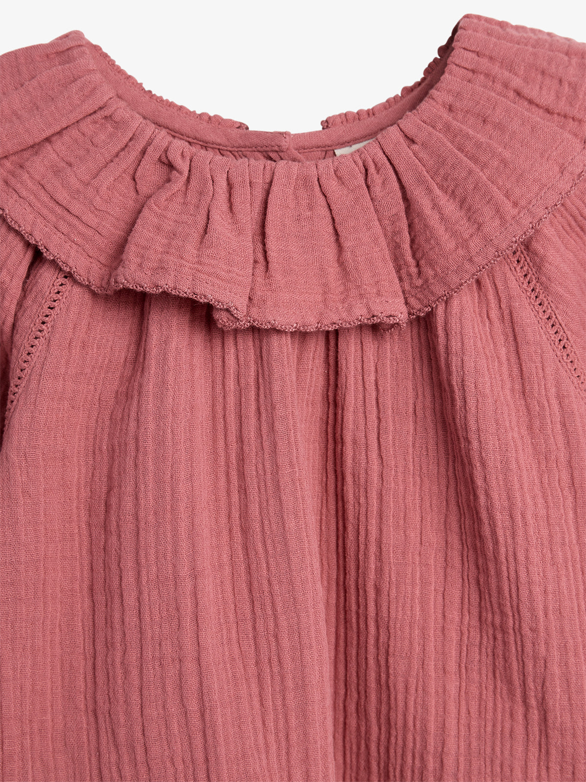 Pink ruffled fabric forms the upper part of a garment with gathered pleats, in a soft texture, suggesting a delicate, possibly vintage style, set against a simple background.