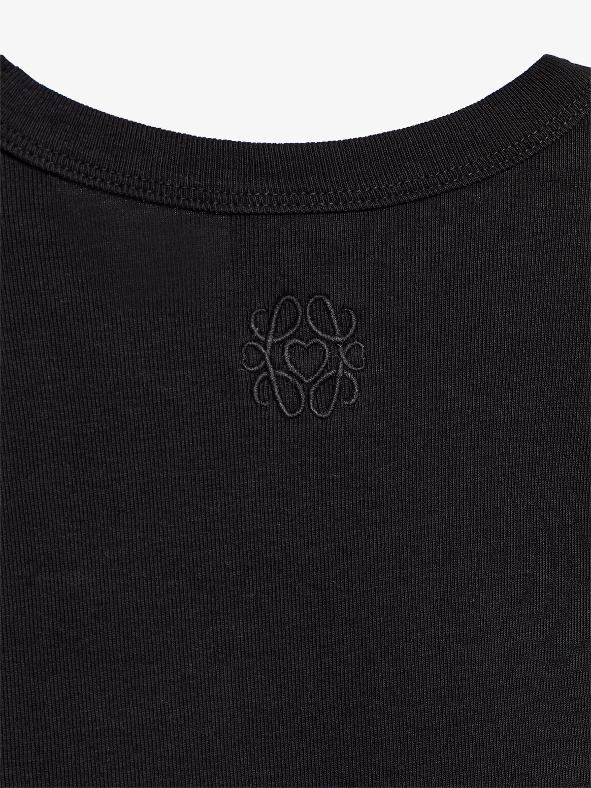 A black garment features an embroidered logo in the center below the collar. The intricate logo design includes looping curves, adding a decorative touch against the plain fabric background.
