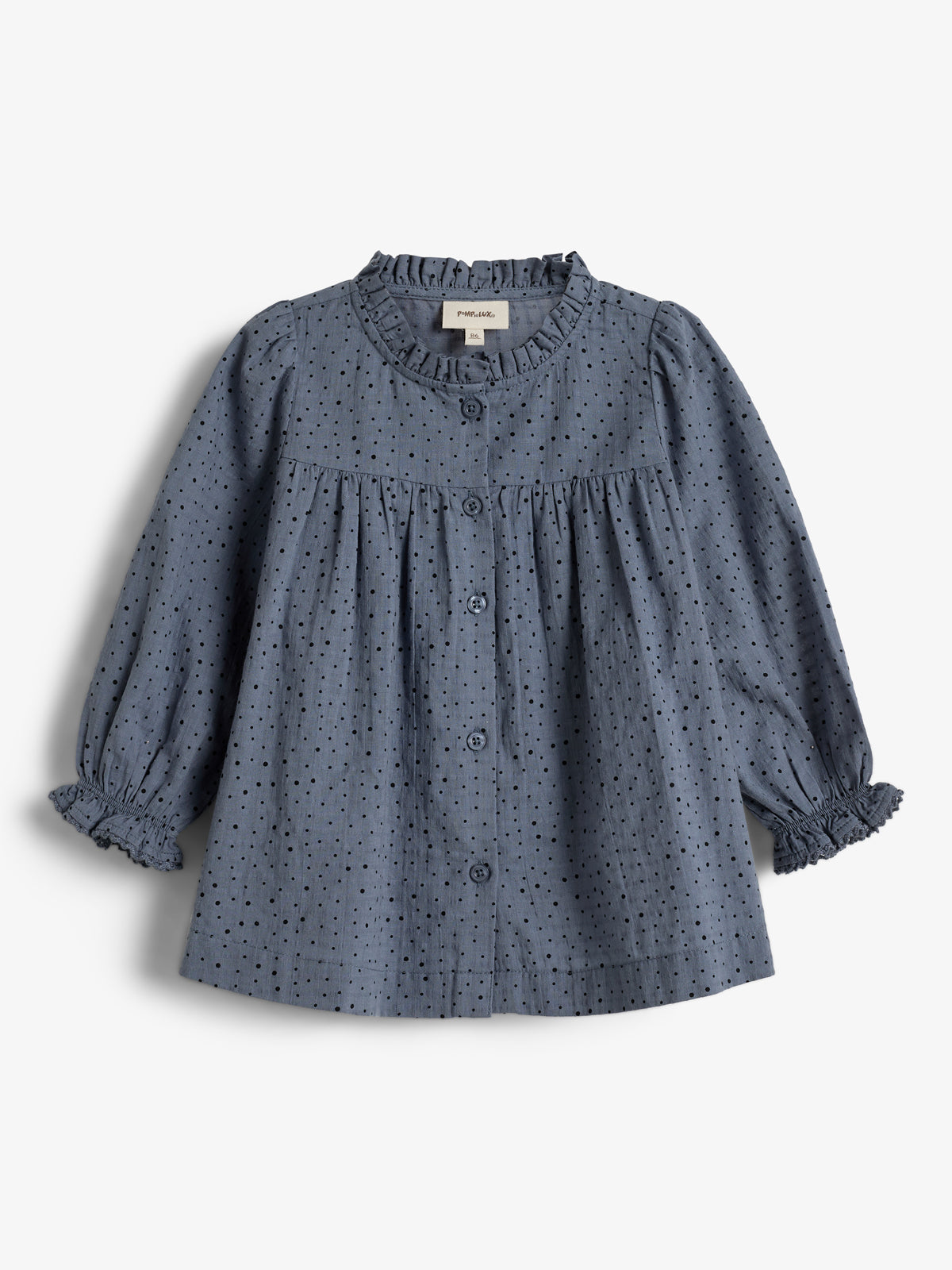 Eine blaue, gepunktete Bluse mit langen Ärmeln und Rüschen an Kragen und Manschetten liegt flach in einem neutralen Umfeld. Hergestellt von "name it", Größe 104.